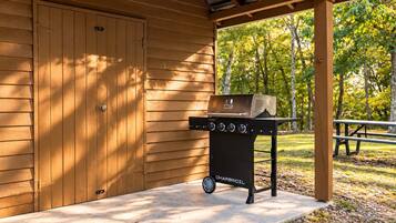 Ein Grill mit Rädern, eine überdachte Terrasse und ein Holzgebäude im Hintergrund.