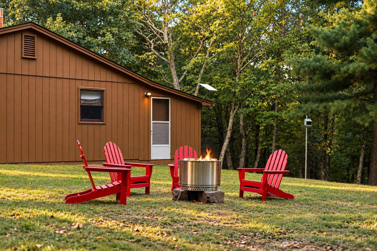 A cabin with a fire pit and red Adirondack chairs in front.
