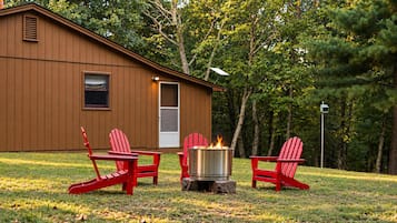 A cabin with a fire pit and red Adirondack chairs in front.
