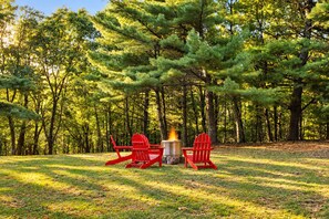 A campsite with two red chairs and a fire pit surrounded by trees.