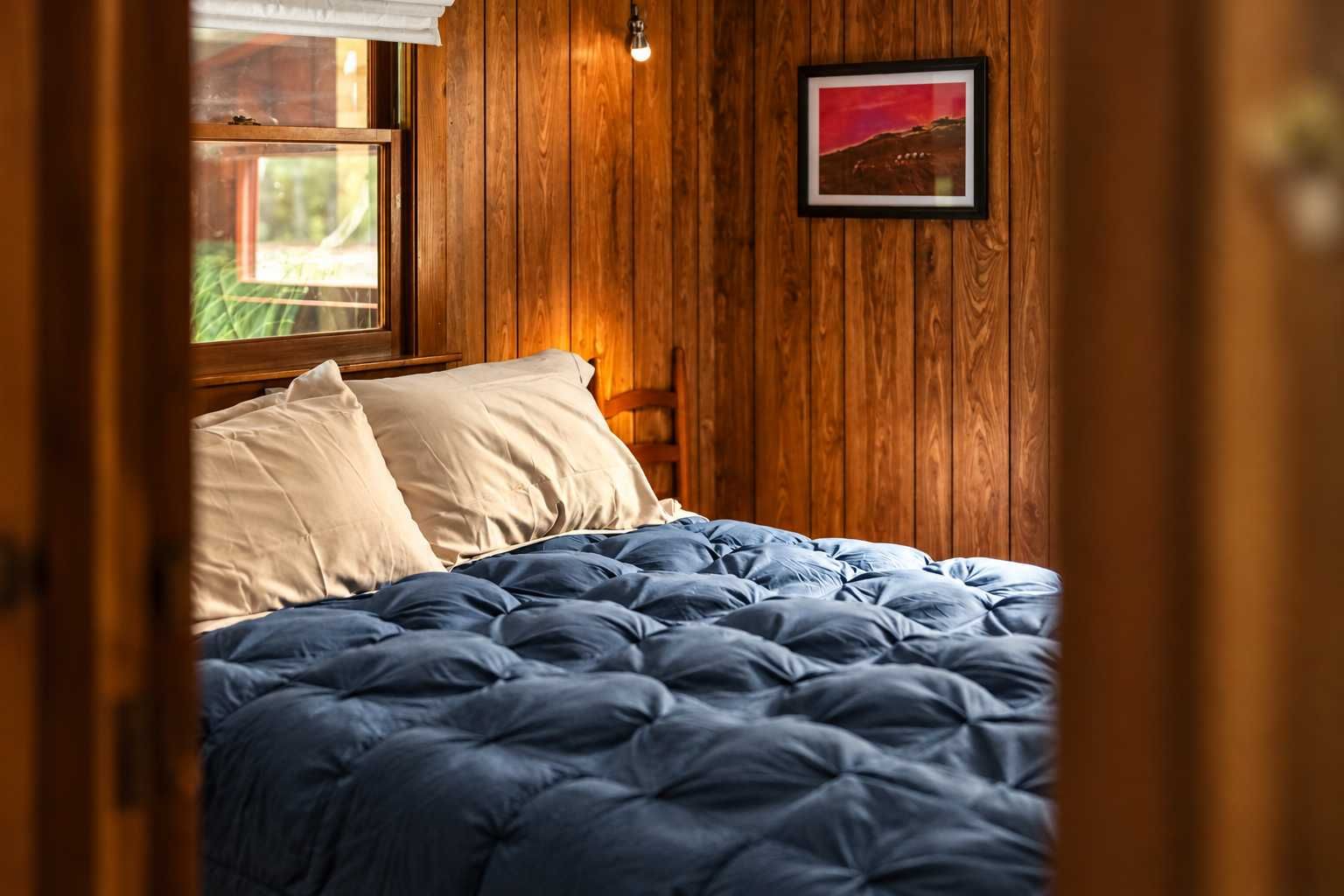 A bedroom with a wooden wall, a bed with blue bedding, and a framed picture on the wall.