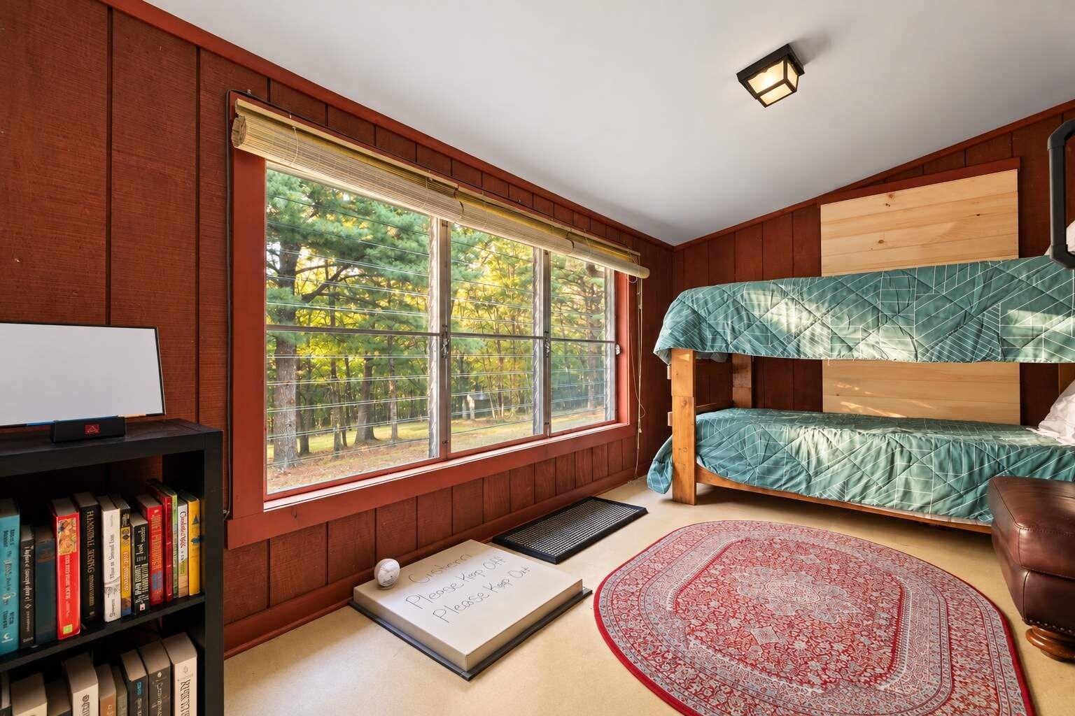 Une chambre avec un lit superposé, une bibliothèque, une fenêtre donnant sur des arbres et un tapis.