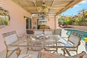 Eine Außenpatio mit einem Glastisch, Korbstühlen, einem Deckenventilator und einem Pool.