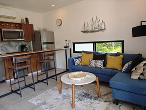 A modern kitchen with a microwave, refrigerator, and a coffee maker. There is a dining area with a blue sofa and a small round table. - Chic Coastal Sanctuary 1-BR condo steps from the beach w/Private Terrace (Santa Cruz Huatulco)