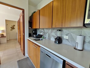 A modern kitchen with wooden cabinets, a dishwasher, a coffee maker, and a blender. - Chic Coastal Sanctuary 1-BR condo steps from the beach w/Private Terrace (Santa Cruz Huatulco)