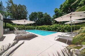 A swimming pool with lounge chairs and umbrellas, surrounded by greenery and a building. - Chic Coastal Sanctuary 1-BR condo steps from the beach w/Private Terrace (Santa Cruz Huatulco)