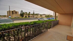 A balcony with a view of a street, a parked car, and a building in the background. - Beachview Condos #103 - Popular Family Retreat Just 30 Seconds from the Sand (South Padre Island)