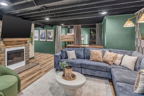 A modern living room with a sectional sofa, a fireplace, and a dining area. - NEW - Maple Retreat - Hot Tub, Games, 8 min to NRG (Fayetteville)