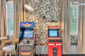 Two arcade machines, a wooden chair, and a window with curtains. - NEW - Maple Retreat - Hot Tub, Games, 8 min to NRG (Fayetteville)