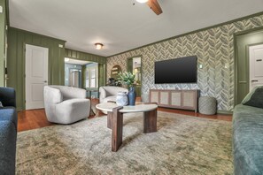 A living room with a flat-screen TV, a coffee table, and a sofa. - NEW - Maple Retreat - Hot Tub, Games, 8 min to NRG (Fayetteville)