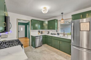 A modern kitchen with green cabinets, stainless steel appliances, and a built-in dishwasher. - NEW - Maple Retreat - Hot Tub, Games, 8 min to NRG (Fayetteville)