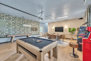 A pool table with a billiard cue, a dartboard, and a pinball machine in a room with a wooden floor and a patterned wall. - NEW - Maple Retreat - Hot Tub, Games, 8 min to NRG (Fayetteville)