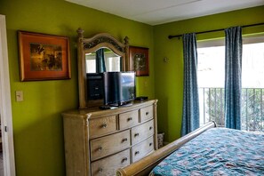 Quarto com cama, penteadeira, televisão e duas fotografias emolduradas na parede.