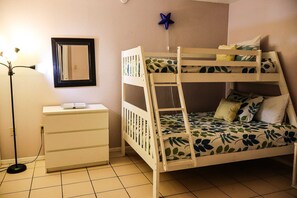 A bunk bed with leaf-patterned bedding, a bedside table, a lamp, and a mirror on the wall. - Beachview Condos #105 - "One of a Kind" Family Retreat Steps from the Gulf (South Padre Island)