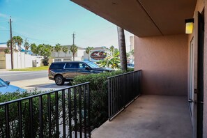 A balcony with a view of a street, a parked SUV, and a building with a sign that reads 'Beach View Condominiums'. - Beachview Condos #105 - "One of a Kind" Family Retreat Steps from the Gulf (South Padre Island)