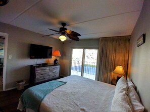 A hotel room with a bed, a television, a ceiling fan, and a view of the outside. - Beachview Condos #206 - Popular 2-BR Retreat with Pure Water & Netflix (South Padre Island)