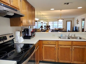 A modern kitchen with wooden cabinets, a black stove, a white countertop, and a large sink. - Beachview Condos #208 - Spacious 2-BR Retreat Just 30 Seconds from the Beach (South Padre Island)