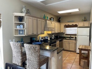 A kitchen with light wooden cabinets, a central island with seating, a refrigerator, and a stove. - Spacious 4-Bedroom South Padre Island Beach House - Steps from the Sand (South Padre Island)