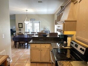 Uma cozinha com ilha central, armários de madeira, fogão e área de refeições com cadeiras e mesa.