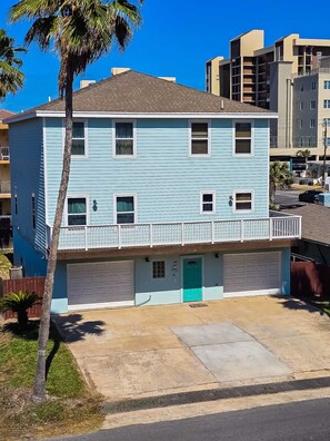 A two-story residential building with a garage, a balcony, and a small front yard. - Spacious 4-Bedroom South Padre Island Beach House - Steps from the Sand (South Padre Island)