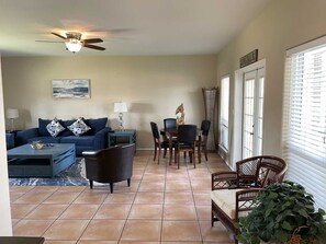 A living room with a sofa, coffee table, and chairs, a dining area with a table and chairs, and a large window with blinds. - Spacious 4-Bedroom South Padre Island Beach House - Steps from the Sand (South Padre Island)