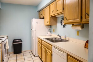A compact kitchen with a refrigerator, sink, and wooden cabinets. - Campeche Townhouse - Spacious 2-BR Home with Private Backyard Near the Beach (South Padre Island)