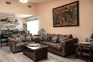 A living room with a brown sofa set, a glass coffee table, and a large abstract painting on the wall. - Campeche Townhouse - Spacious 2-BR Home with Private Backyard Near the Beach (South Padre Island)