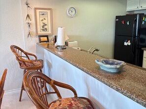 A kitchen with a granite countertop, two wooden chairs, a clock, and a refrigerator. - Continental #101 - Ground-Floor Beachfront Luxury Steps from the Gulf (South Padre Island)