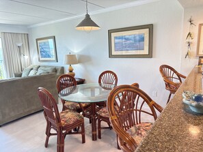 A dining area with a round glass table surrounded by wooden chairs with floral upholstery, a hanging pendant light, and framed artwork on the walls. - Continental #101 - Ground-Floor Beachfront Luxury Steps from the Gulf (South Padre Island)