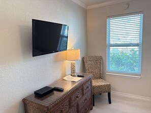 A room with a mounted flat-screen TV, a wicker desk with a lamp, and a chair. - Continental #101 - Ground-Floor Beachfront Luxury Steps from the Gulf (South Padre Island)