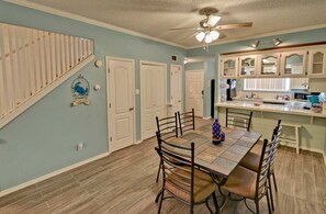 A dining area with a wooden table and chairs, a ceiling fan, and a kitchen with white cabinets. - Dolphin #23 - Spacious Families-Only Retreat Across from the Beach (South Padre Island)