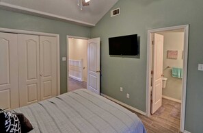 Une chambre à coucher avec un lit, un téléviseur fixé au mur et une porte donnant sur une salle de bain.