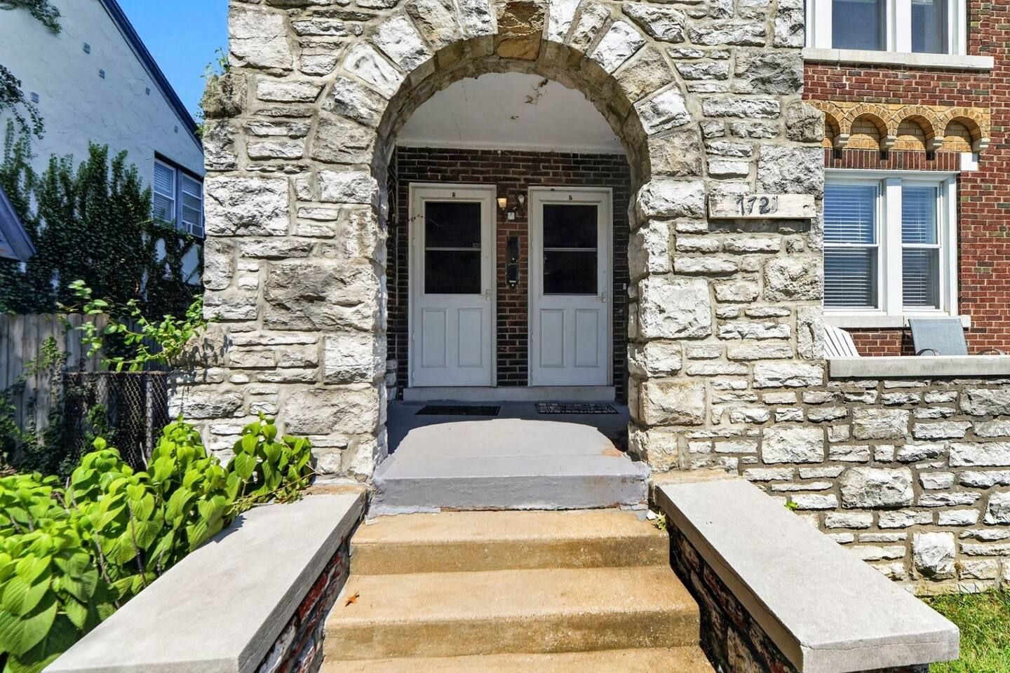 A stone facade with a central doorway, a small porch, and a brick wall with a window.