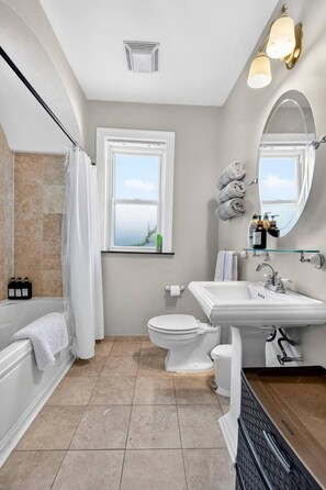 Ein Badezimmer mit Badewanne, Toilette und Waschbecken. Ein Fenster mit Aussicht, ein Spiegel und eine Duschvorhang sind vorhanden.