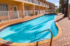 A swimming pool with a tiled edge, surrounded by a brick walkway, and adjacent to a building with balconies. - Dolphin 28 - Spacious Families-Only Retreat Across from the Beach (South Padre Island)