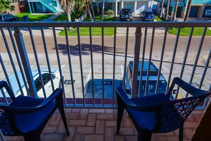 A balcony with a view of parked cars and a building in the background. - Dolphin 28 - Spacious Families-Only Retreat Across from the Beach (South Padre Island)