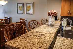 A kitchen with a granite countertop, wooden chairs, a vase with flowers, and a sink. - Edgewater #506 - Peaceful 2-BR Families-Only Beachfront Sanctuary (South Padre Island)