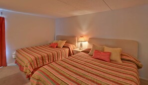 Une chambre d’hôtel avec deux lits, chacun doté de draps à rayures et de plusieurs oreillers. Il y a une table de chevet avec une lampe entre les deux lits.