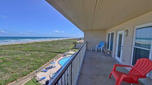 Un balcon avec vue sur la plage, une piscine et une chaise rouge.