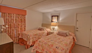 A hotel room with two beds, a nightstand, a lamp, and a door. - Premier 3-BR Family Escape at Edgewater #507 - Spectacular Corner Gulf Views (South Padre Island)