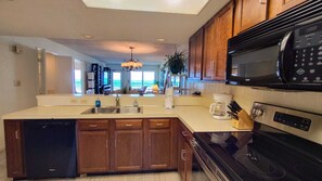 A modern kitchen with wooden cabinets, a dishwasher, a stove, and a microwave. - Updated Beachfront Escape at Embassy #402 - Intimate 30-Unit Complex (South Padre Island)