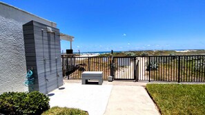A gated patio area with a view of the beach, a concrete bench, and a small table. - Updated Beachfront Escape at Embassy #402 - Intimate 30-Unit Complex (South Padre Island)