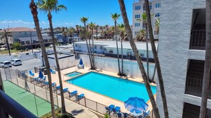 A swimming pool with lounge chairs and umbrellas, surrounded by palm trees and buildings. - Updated Beachfront Escape at Embassy #402 - Intimate 30-Unit Complex (South Padre Island)