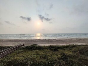 Una playa con un pasillo de madera que conduce a la orilla, un cielo nublado y el océano.