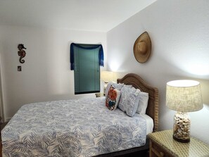 Ein Schlafzimmer mit einem Bett, einem Nachttisch, einer Lampe, einem an der Wand befestigten Hut und einer dekorativen Meeresschnecke.