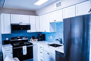 Et moderne køkken med hvide skabe, et rustfrit stål køleskab, en sort komfur og en backsplash med blå fliser.