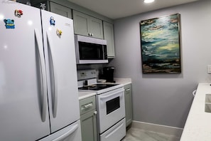 Una cocina equipada con refrigerador, microondas, estufa y un cuadro en la pared.