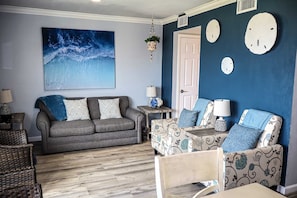 A living room with a grey sofa, patterned armchairs, a blue wall, and a large abstract painting. - La Internacional #205 - Views of the Gulf Pet-Friendly SPI Beachfront Condo (South Padre Island)
