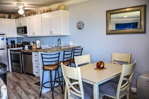 A compact kitchen with white cabinets, a microwave, a sink, and a dining area with a table and chairs. - La Internacional #205 - Views of the Gulf Pet-Friendly SPI Beachfront Condo (South Padre Island)