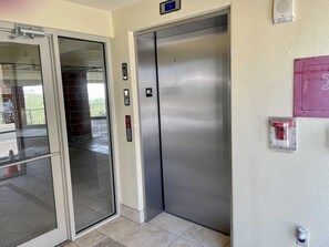 Ein Aufzug mit digitaler Anzeige, Brandmelder und an der Wand befestigtem Feuerlöscher.